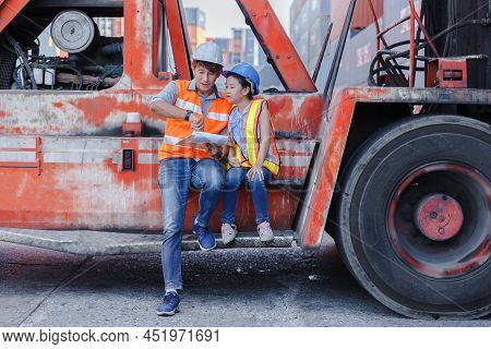 Man Engineering And Daughters Sitting On Forklift Working With Clipboard In Container Yard. Work Edu