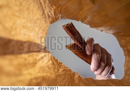 A Hand Places A Pet Treat In A Paper Bag. A Mature Man's Hand Holds A Dried Bully Sticks For Dogs Ov