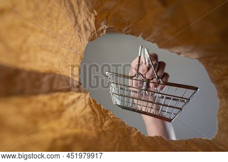 A Hand Places A Shopping Cart In A Paper Bag. A Mature Man's Hand Holds An Empty Shopping Cart Over 