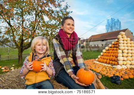 Happy Mother And Child Sitting On Haystack With Pumpkins