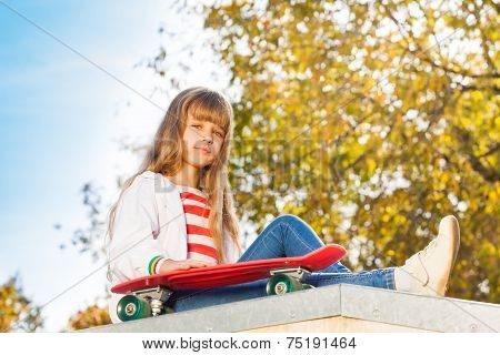 Blond girl with long hair sits near skateboard