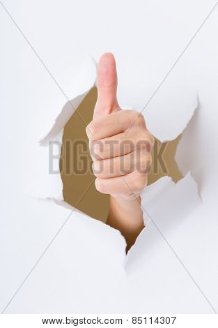 Hand with thumb up through a hole in paper