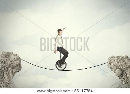Brave business man riding an mono cycle between cliffs concept