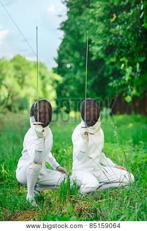 Two fencers women squatting down with rapiers pointing up ready for competition