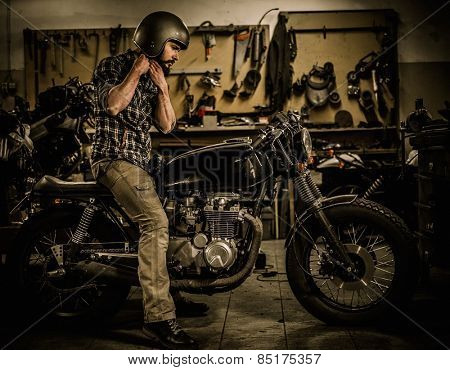 Rider and his vintage style cafe-racer motorcycle in customs garage 