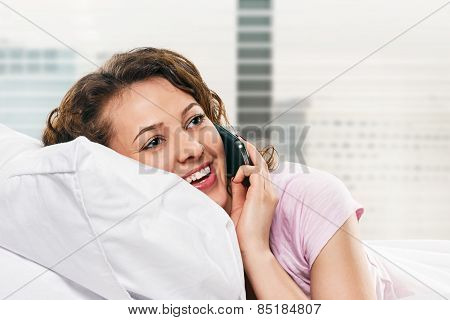 Radiant woman with phone lying on bed