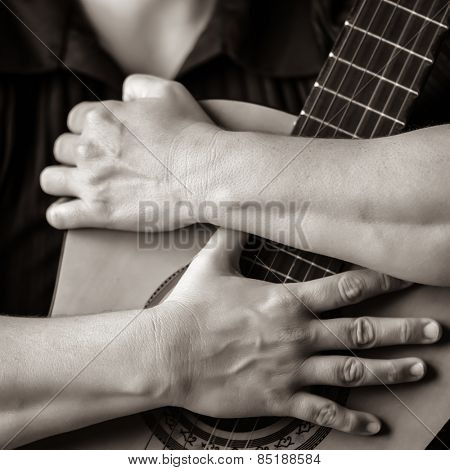 Classic guitar closeup in sepia - Musician hands embracing a classic acoustic guitar