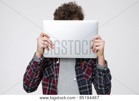 Young man covering face with laptop over gray background