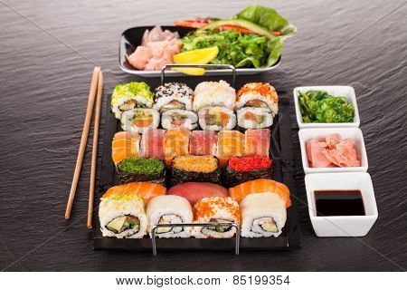 Delicious sushi rolls served on black plate and stone