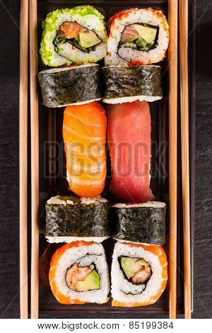 Delicious sushi rolls served on black plate and stone