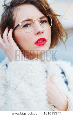 Young Beautiful Short-sighted Girl In A White Jacket Stares Through His Glasses At A City Street, Cl