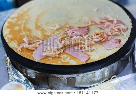 Making ham and cheese crepe at pan. Salty crepe or pancake with fillings made by street vendor's hands at outdoors creperie. French cuisine, cooking for commercial kitchen.