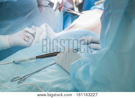 Close-up image of surgeon putting on stitches during cosmetic surgery in hospital operating room. Doctor holding forceps stitching the patient up. Breast augmentation enlargement enhancement. Breast implant plastic surgery.