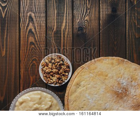 Ingredients for baking a cake, top view on wooden board. shortcakes, buttercream or cream and nuts on a plate on vintage wooden kitchen table. copyspace for cook recipe.