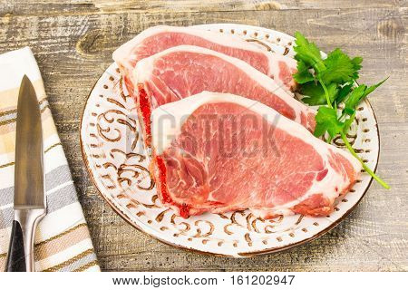 A white plate of raw sliced meat on wooden table top view. Food a knife branches of greens