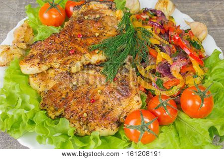 Pork steak with a fork lettuce tomatoes and dill close-up view. Grey food background on wooden table