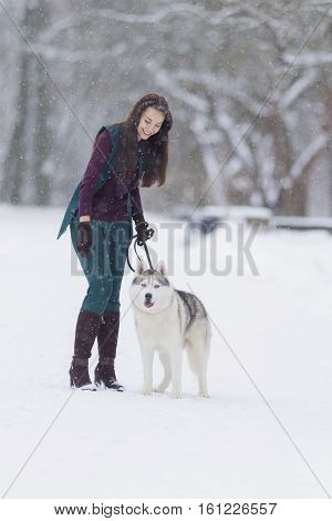 Human and Pet Relationships Ideas and Concepts.Lovely Caucasian Brunette Woman Along With Her Husky Dog Walking Outdoors in Winter Forest. Vertical Image Composition