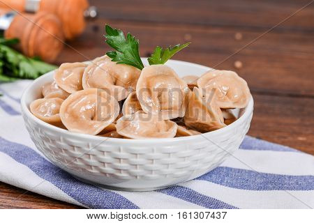 Boiled prepared homemade russian dumplings or pelmeni with beef meat on the white plate with fresh parsley