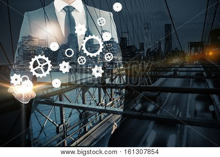 Businessman holding abstract cogwheels on city background. Double exposure. Industry concept