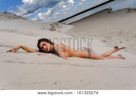 Portrait of beautiful naked woman relaxes on sand coast with seaweed