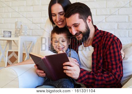 Close-up of happy family, spending time together. Loving wife and mum embracing her dearest while spending time when reading a book. The concept of togetherness 