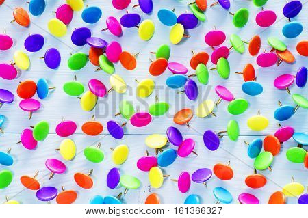 Colorful push pins on blue wooden background close up. Bright multi-colored thumbtacks.