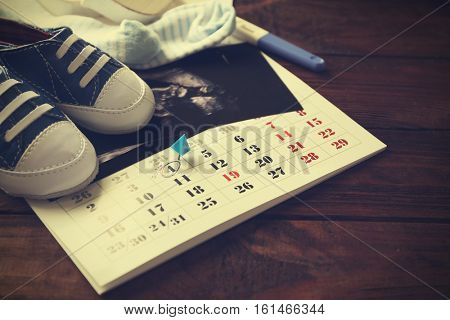 Calendar with ultrasound scan of baby and children shoes, closeup