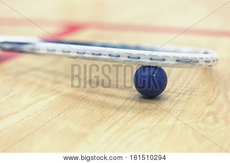 Close up of a squash racket and ball on the wooden background. Racquetball equipment. Squash ball between squash racket and floor on the court. Photo with toning and selective focus