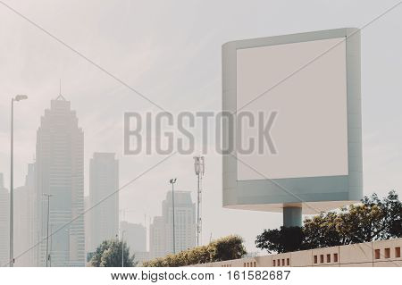 Mock up of blank vertical white advertising billboard in Dubai with residential and office modern contemporary skyscrapers and clean sky behind plants and stone wall below