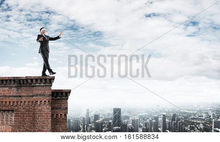 Businessman with blindfolder on eyes walking on building top