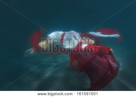 Woman in red dress dancing underwater in the pool.