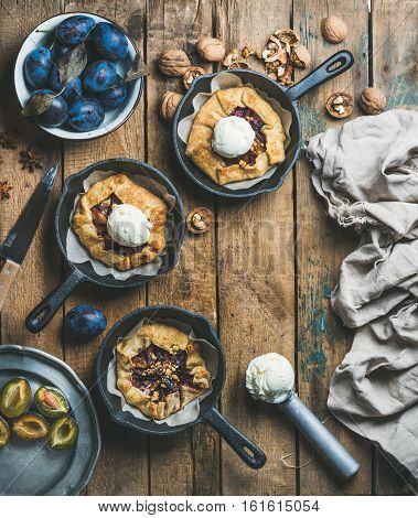 Plum and walnut crostata pie with ice-cream scoops in individual cast iron pans over rustic wooden table, top view, copy space. Slow food concept