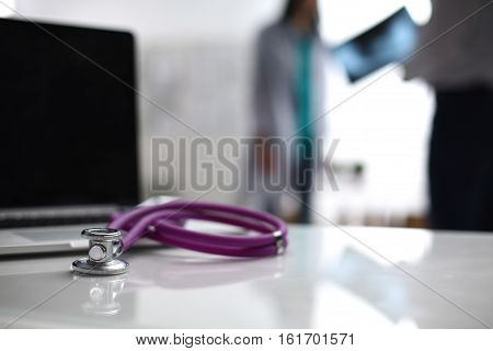 Laptop and stethoscope on the desk doctors standing in the background.