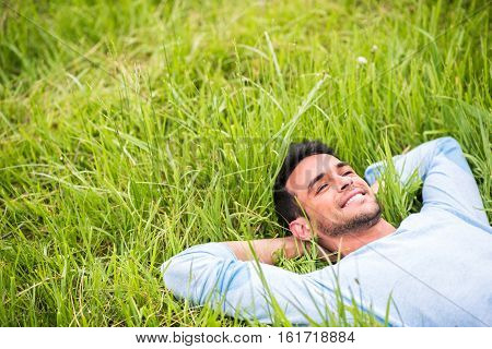 Smiling pretty young man lying dreaming and relax on the green grass