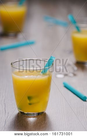 Freshly squeezed orange juice in glass with blue straw and ice cubes. Selective focus on front glass and straw.