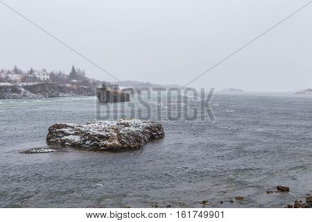 Cold winter blizzard causes heavy snow fall on rocky islands in the Olfusa river at Selfoss Iceland.
