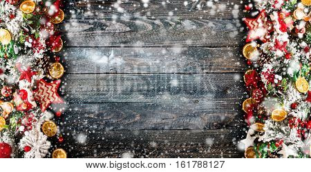 Merry Christmas Frame with Snow and wood green pine, colorful baubles, knots with berries,stars, orangesand other seasonal stuff over an old wooden aged background