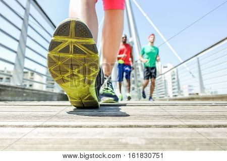 Close up of woman legs running with friends in urban wood city bridge - Young people doing jogging in sunny day - Healthy lifestyle concept - Focus on top left foot - Warm vivid filter