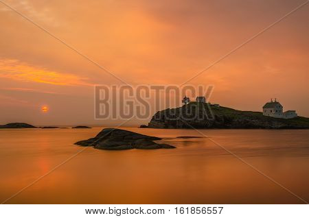 Orange sunset on Fjoloy Fort coast and lighthouse Norway