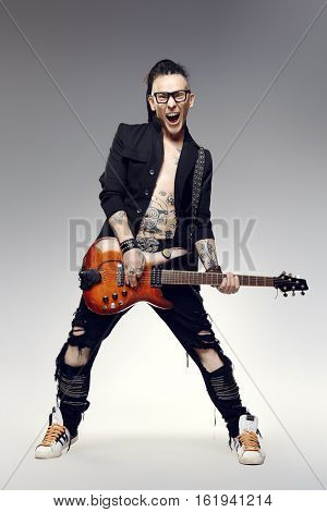 Excited rock musician is playing electrical guitar. Full length studio shot. Entertainment and musical concept. 