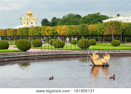 Peterhof, Saint - Petersburg, Russia - August 19, 2016: People walk in The Upper Garden. On the background is The Palace Church of Saints Peter and Paul. Foreground is fragment of The Mezheumny (Indefinite) Fountain.