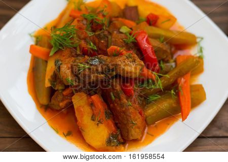 Stew with potatoes, carrots, pickles, tomatoes and hot peppers. Azu by Tartarian on a white square plate. Wooden rustic background. Top view