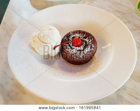 Tasty sweet  chocolate lava cake dessert with cherry top and vanilla ice cream served on white plate