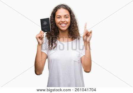 Young hispanic woman holding passport of Australia surprised with an idea or question pointing finger with happy face, number one