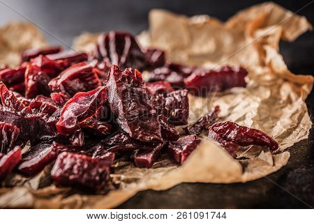A Pile Of Dried Beef Jerky Pieces On Paper And Cutting Board
