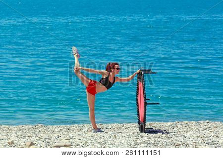 A Slim Athletic Girl With Dreadlocks Doing Exercises On A Fitness Trampoline Outdoors On A Pebble Be