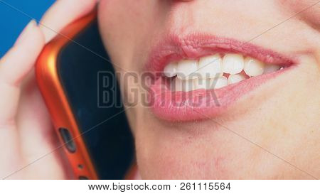 Close-up, Female Lips Without Makeup Talking On A Red Mobile Phone, Against A Blue Background.