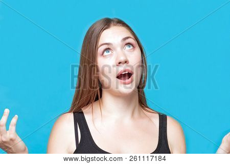 Attractive Young Caucasian Woman With Dark Hair Poses Praying, Hahds And Blue Eyes Up, Mouth Open. A