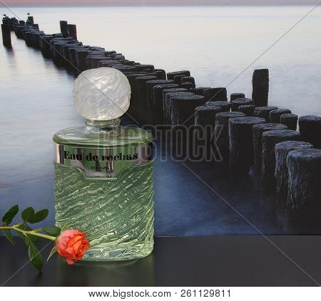 Eau De Rochas, Fragrance For Ladies, Large Perfume Bottle In Front Of The Picture Of A Groyne In The
