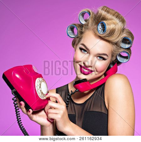 Young girl dials a phone number on an old phone. Young happy woman with blue curlers calling by retro phone.  Portrain of an atractive female using a vintage phone. 